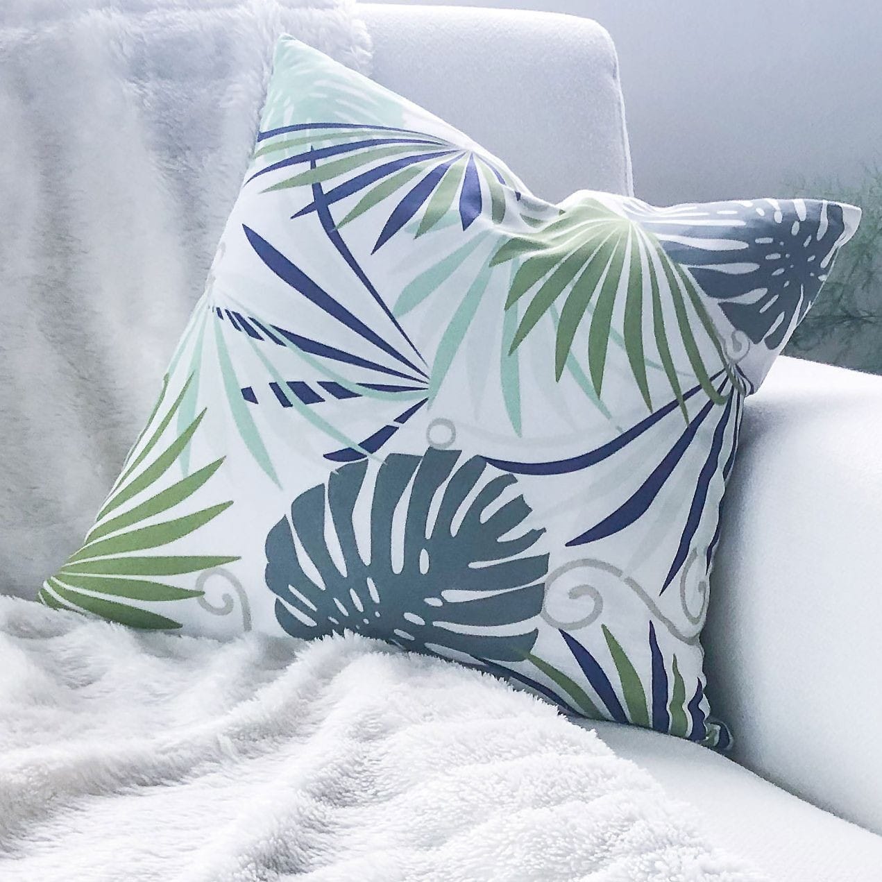 Photo of cushion design white background with green and blue palm leaves and monstera leaves.